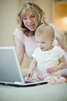 Pregnant woman teaching baby daughter to use laptop