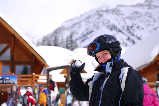 Young girl holding a snowball in front a chalet at downhill ski resort