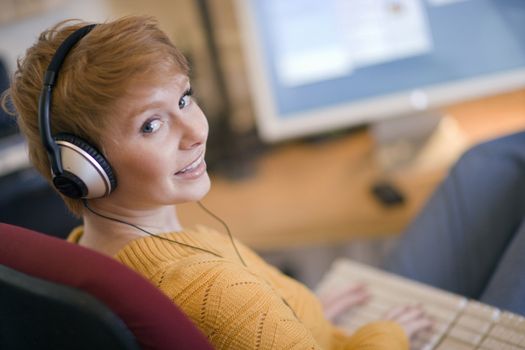 Young smiling woman  listening to headphones at computer
