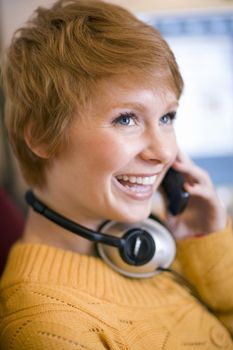 Young smiling woman talking on cell phone with headphones around her neck