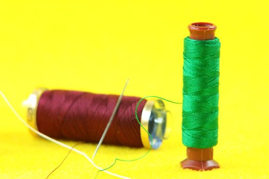 green  string roll needle with redish string in yellow background sewing handcrafted concepts
