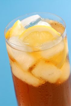Glass of cold lemon iced tea with ice and lemon on blue background