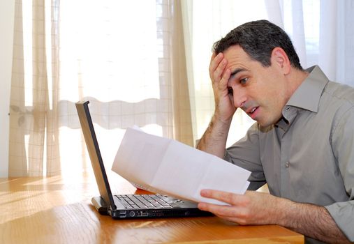 Man sitting at a desk looking at bills with horror
