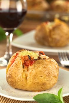 Baked potato with tomato filling and cheese on top with red wine in back (Selective Focus, Focus on the front of potato)