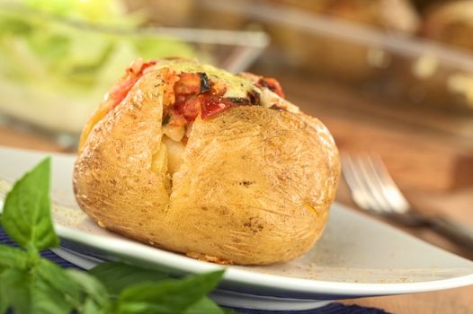 Baked potato with tomato filling and cheese on top (Selective Focus, Focus on the front of potato)