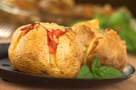 Baked potato with tomato filling and cheese on top on metal plate garnished with basil leaf (Selective Focus, Focus on the front of potato)