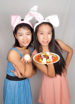 Cute Asian bunny girls hold plate of Easter eggs, chocolate and rock egg.