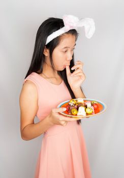 Cute Asian bunny girl hold plate of Easter eggs and chocolate.