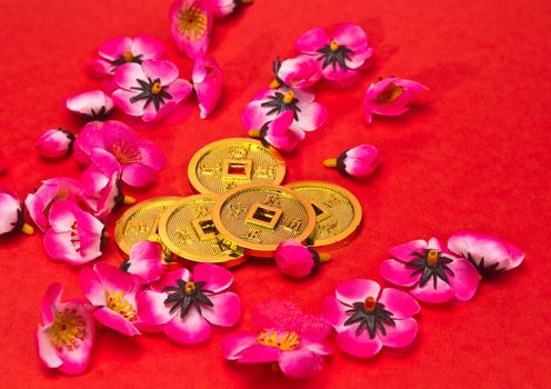 Golden coins ornaments with plastic cherry blossoms on red surface for CNY celebration