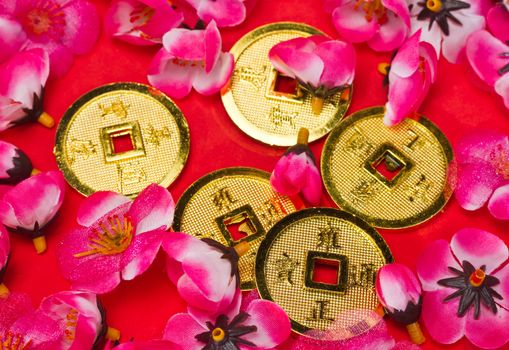 Golden coins ornaments with plastic cherry blossoms on red surface for CNY celebration