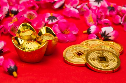 Angled view of Golden nuggets and emperors coins with cherry plum blossoms on red surface for Chinese New Year