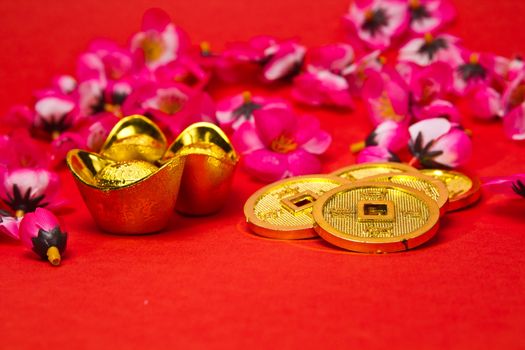 Angled view of Golden nuggets and emperors coins with cherry plum blossoms on red surface for Chinese New Year