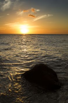 sunset over the calm pacific ocean warming a boulder