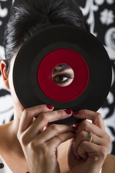 young woman looking through the hole of a small dusty record with a red label