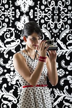 young woman is stylist 60's inspired clothing, holding an instant camera and preparing to take a photo