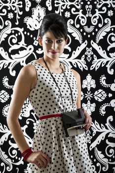 young woman is stylist 60's inspired clothing, holding an instant camera