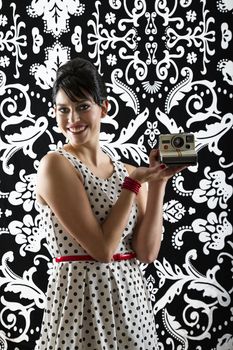 young woman is stylist 60's inspired clothing, presenting an instant camera
