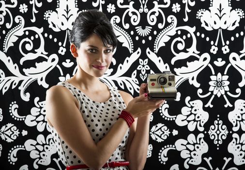 young woman is stylist 60's inspired clothing, presenting an instant camera