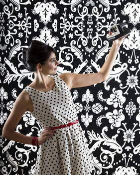 young woman is stylist 60's inspired clothing, taking a self-portrait with an instant camera