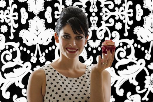 young woman is stylist 60's inspired clothing, holding a velvet cupcake