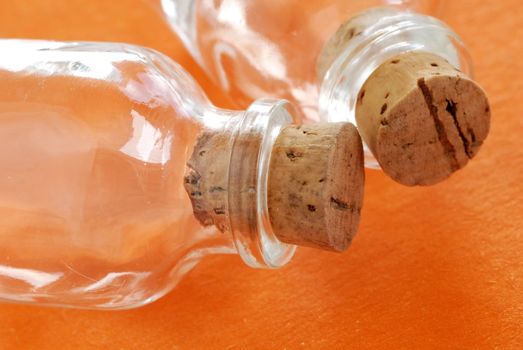 two small empty glass bottles closed with corks over orange background