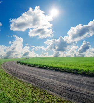 summer landscape with rural road, green field and blue cloudy sky with sun