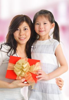 Little beautiful pretty Asian girl giving a gift to her happy mother - indoors.