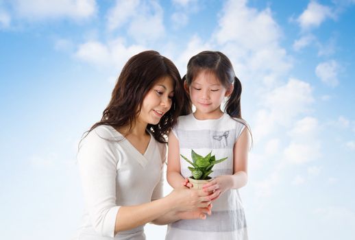 Happy Asian young mother with daughter taking care plant in summer day, blue sky as background.