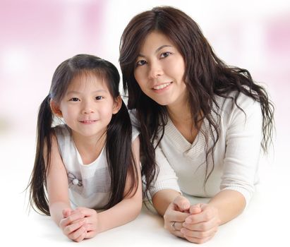 Portrait of a joyful mother and her daughter smiling at the camera. Happy Asian family lying at home.