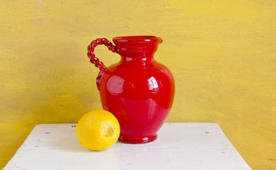 Still life. Red vase and yellow lemon on a shelf.