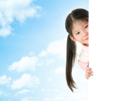 Young Asian girl hiding behind a blank white card in summer day, blue sky as background.