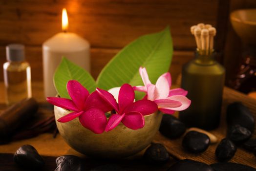 Spa setting with frangipani flower, essential oil, zen stones and aromatic candles on table, Zen concept.