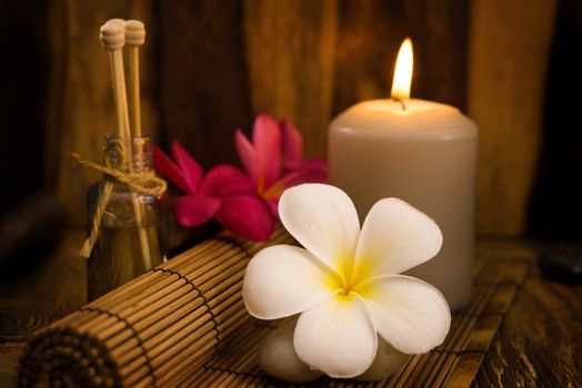 Low light spa setting indoor with candle, frangipani and aroma set.