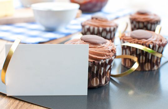 Delicious chocolate easter cupcakes on a baking tray with a gold ribbon decoration and blank card 