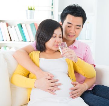 Pregnancy couple healthcare concept. Pregnant woman drinks glass of water at home. 