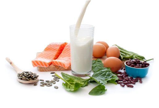 Protein rich foods including eggs, spinach leaves and pumpkin seeds with a glass of pouring milk in the middle