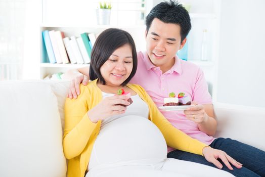 Young Asian pregnant woman and husband eating sweet cake at home