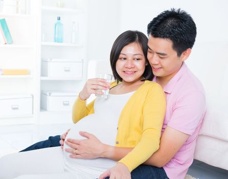 Pregnant woman drinks glass of water at home. Pregnancy couple healthcare concept.