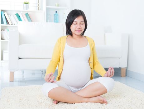 Calm Asian pregnant woman meditating at home.