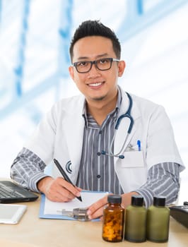 Young Southeast Asian medical doctor working on his desk, inside hospital room.