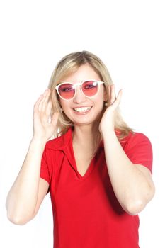 Trendy young blonde woman in red sunglasses beaming happily at the camera isolated on white