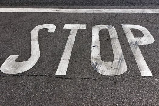 Stop sign painted on the sidewalk and road asphalt with white pedestrian line