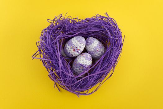 Heart shaped violet nest with Easter decorated eggs on yellow background