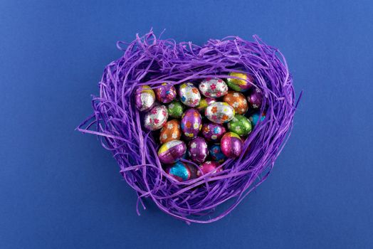 Heart shaped nest with chocolate Easter eggs on blue background