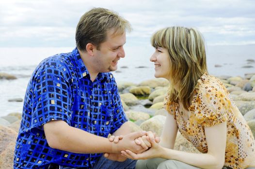 Young couple in love sitting together outdoors in the sea beach