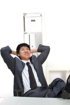Laughing Asian businessman relaxing in his office with his feet up on the desk and his hands behind his head