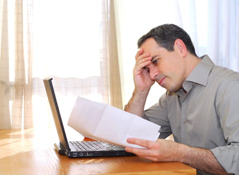 Man sitting at his desk with a laptop and bills  looking concerned