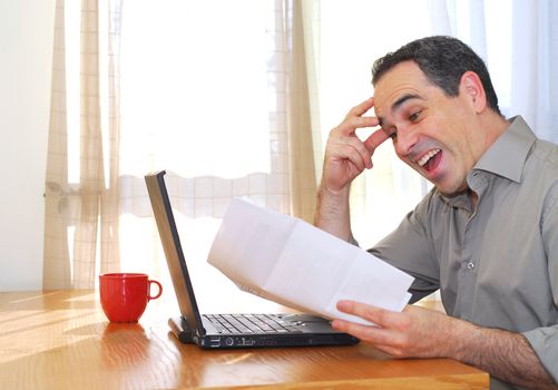 Man sitting at his desk with a laptop and papers looking happy