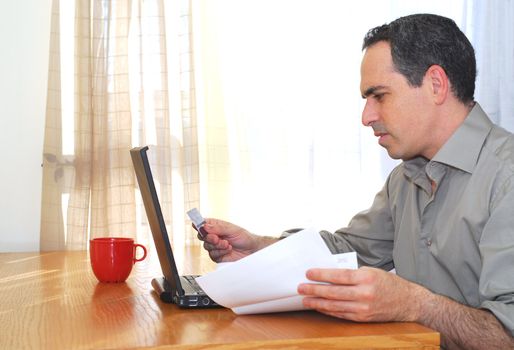 Man sitting at his desk with laptop, papers and credit card