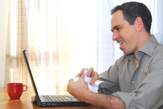 Man sitting at his desk with a laptop crumpling papers